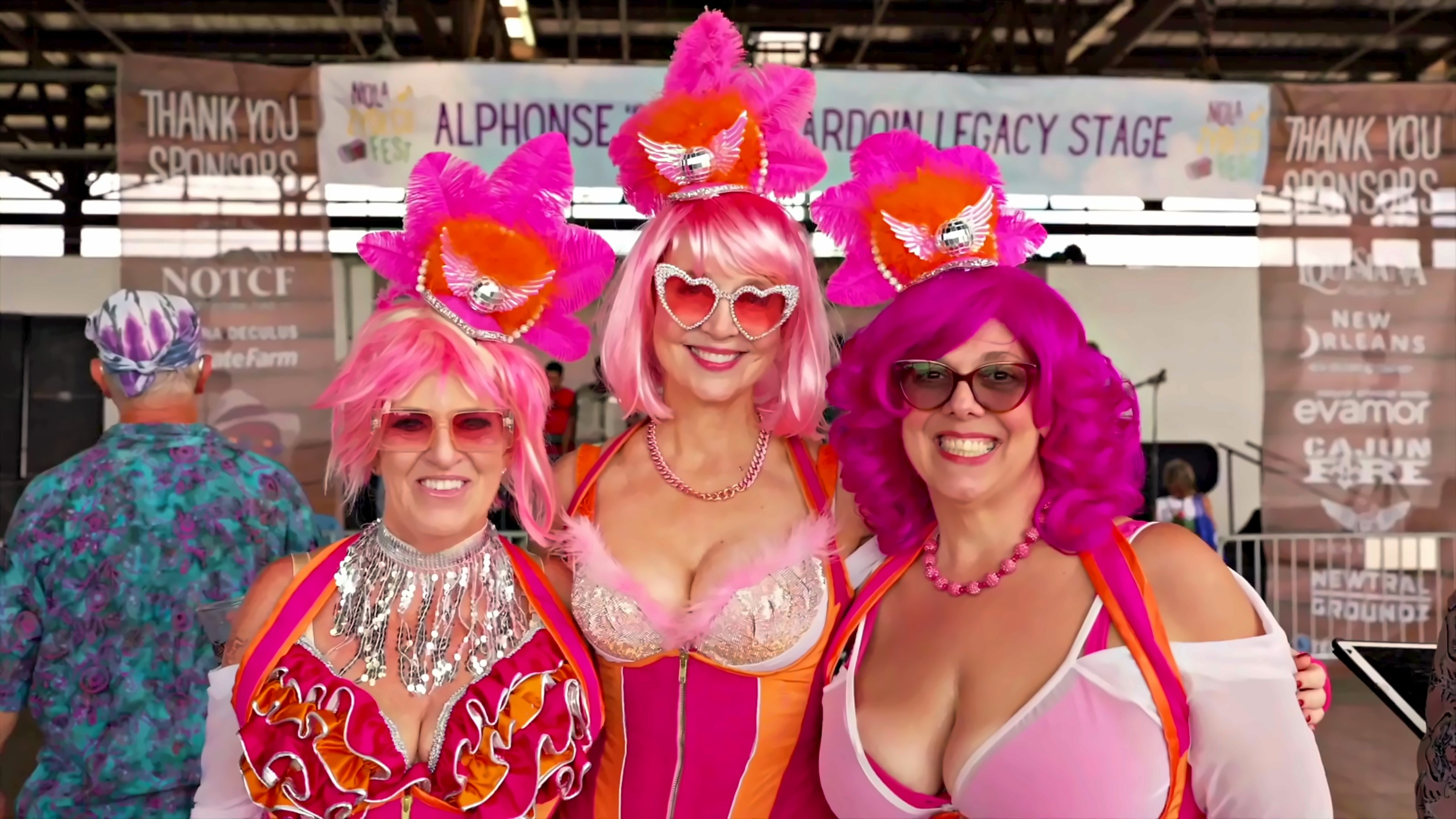 Three festivalgoers in pink feathered costumes in front of the Legacy Stage