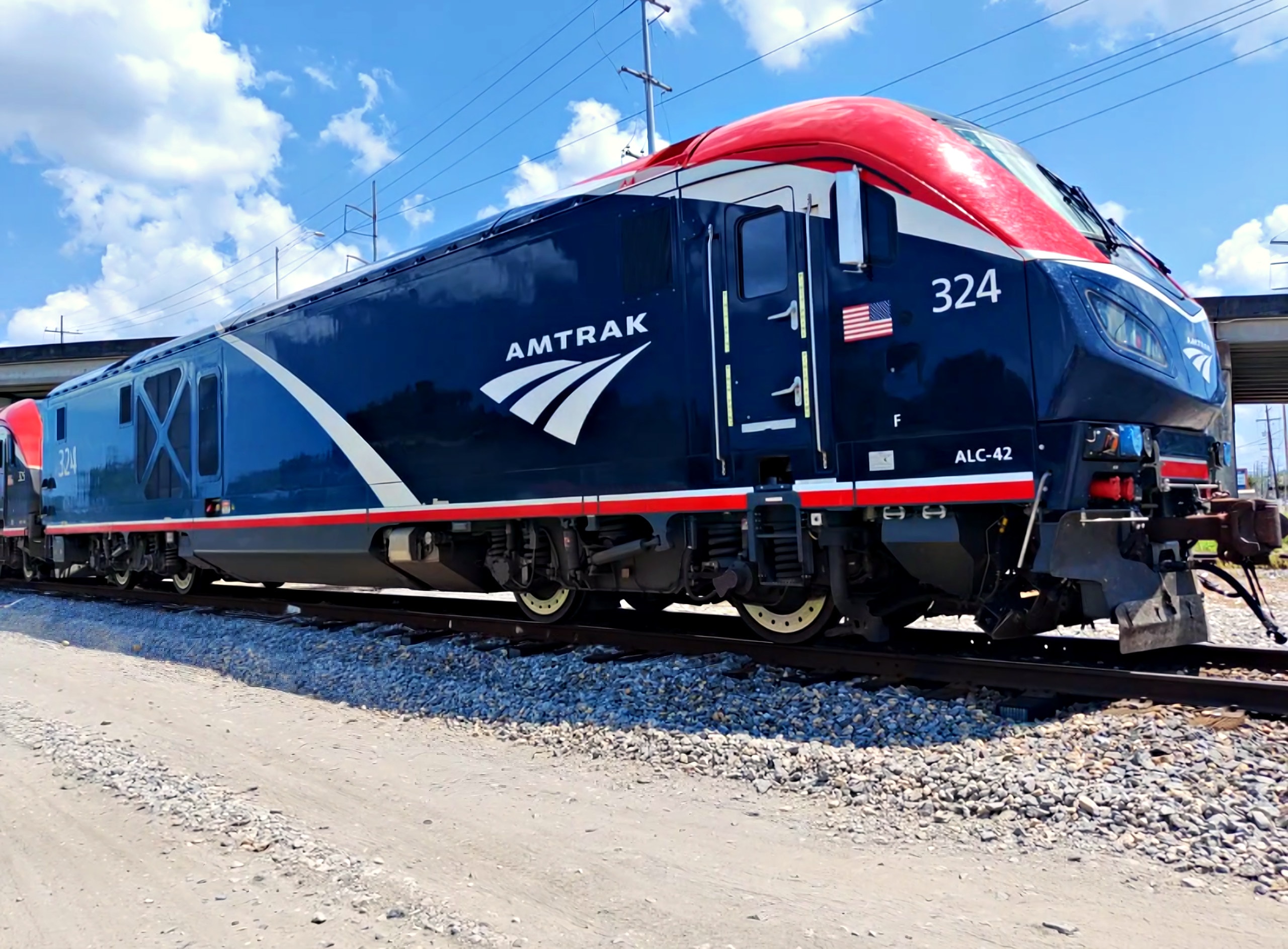 An Amtrak locomotive in red, white, and blue livery on the tracks under a bright blue sky