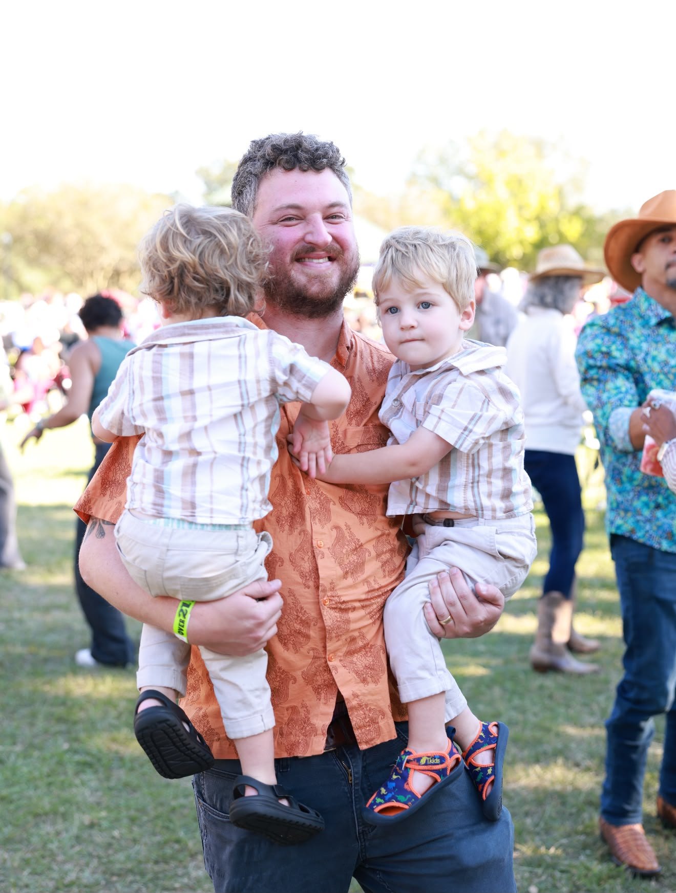 A smiling dad holding his two toddler sons at the festival