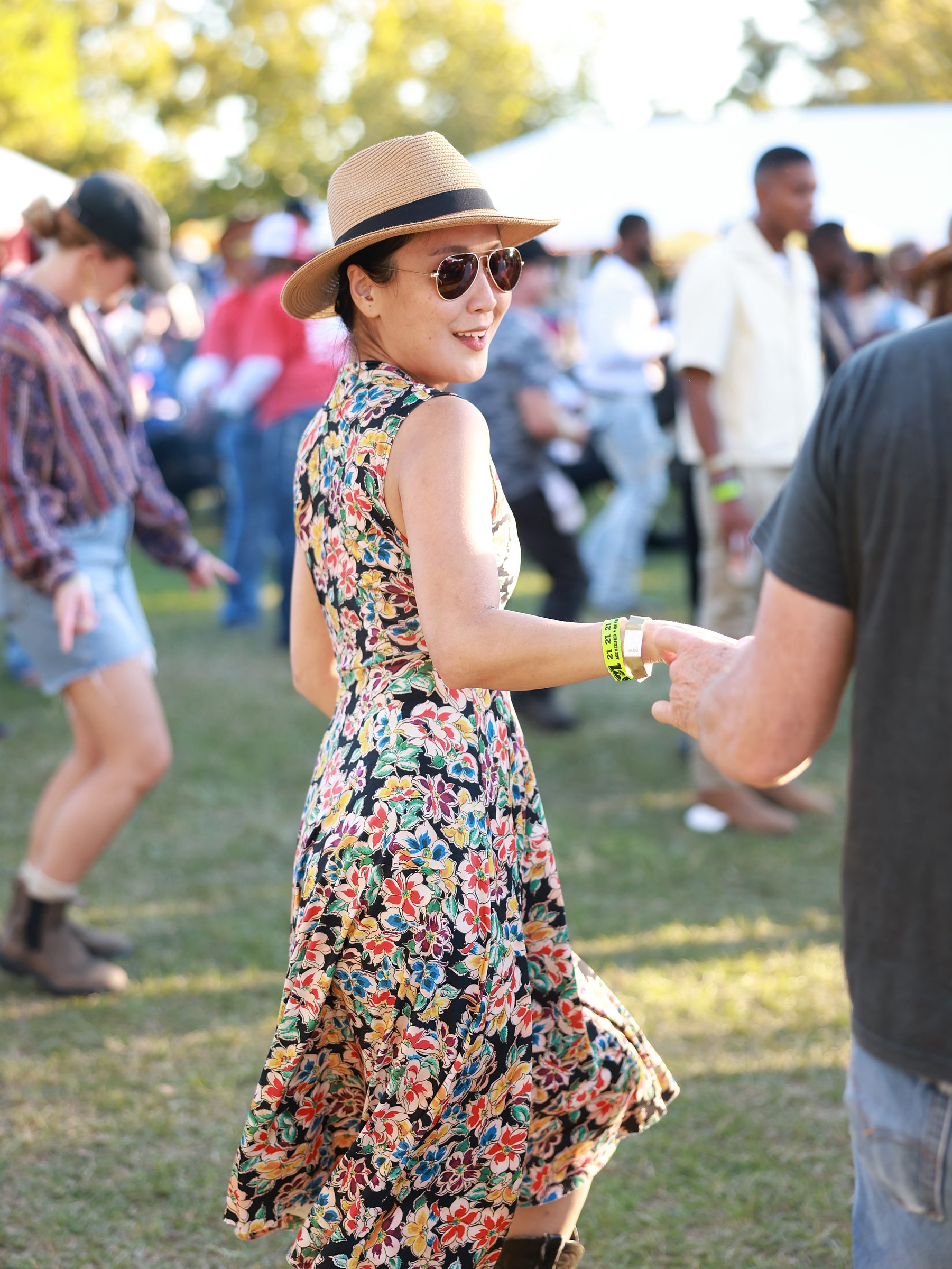 A woman in a floral dress and straw hat dancing with her partner
