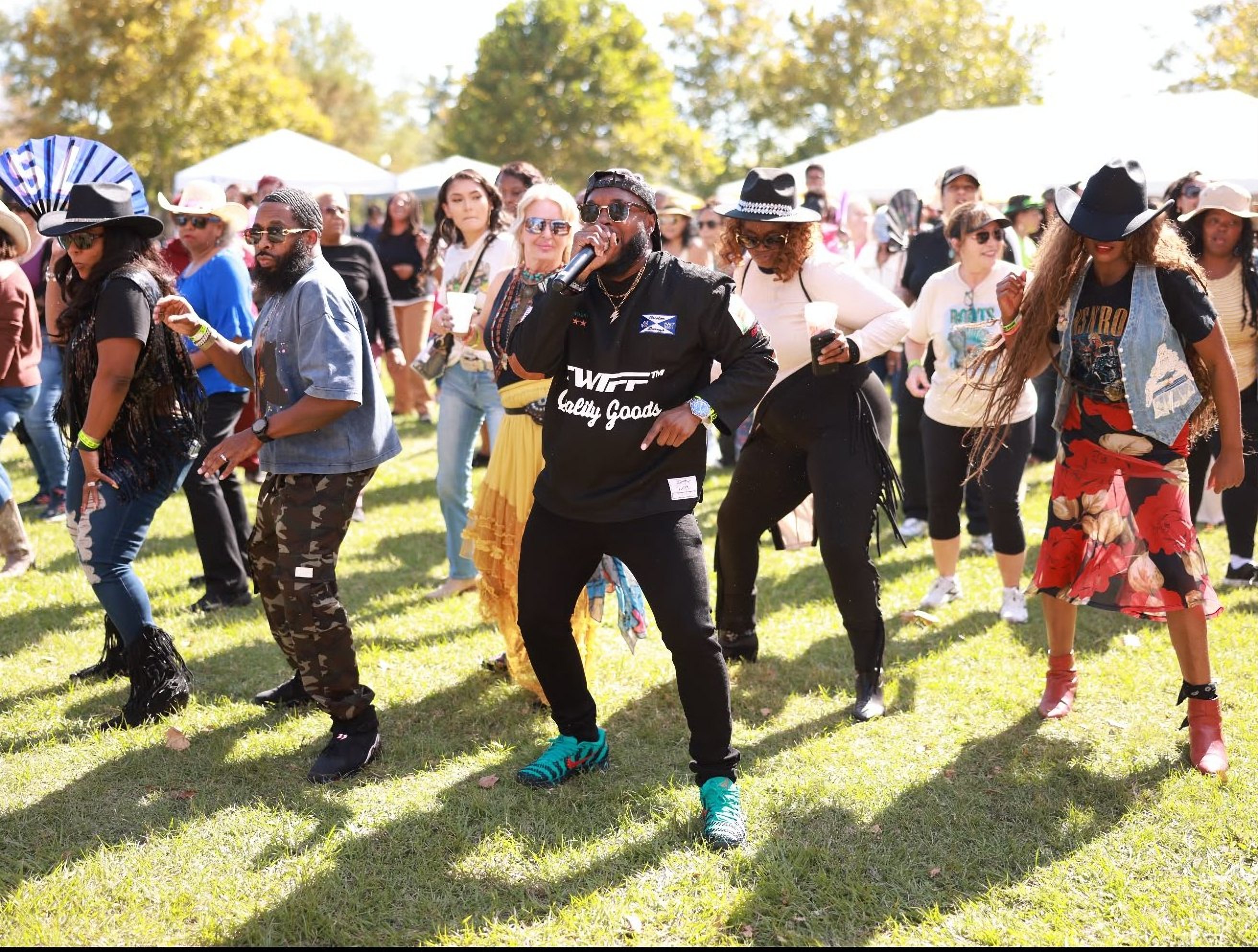 A crowd line dancing on the lawn behind a singer with a microphone