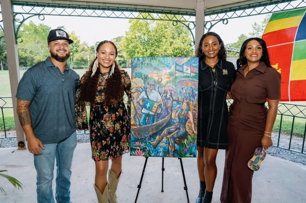 Four people at a park gazebo beside the painted 2026 festival poster on an easel