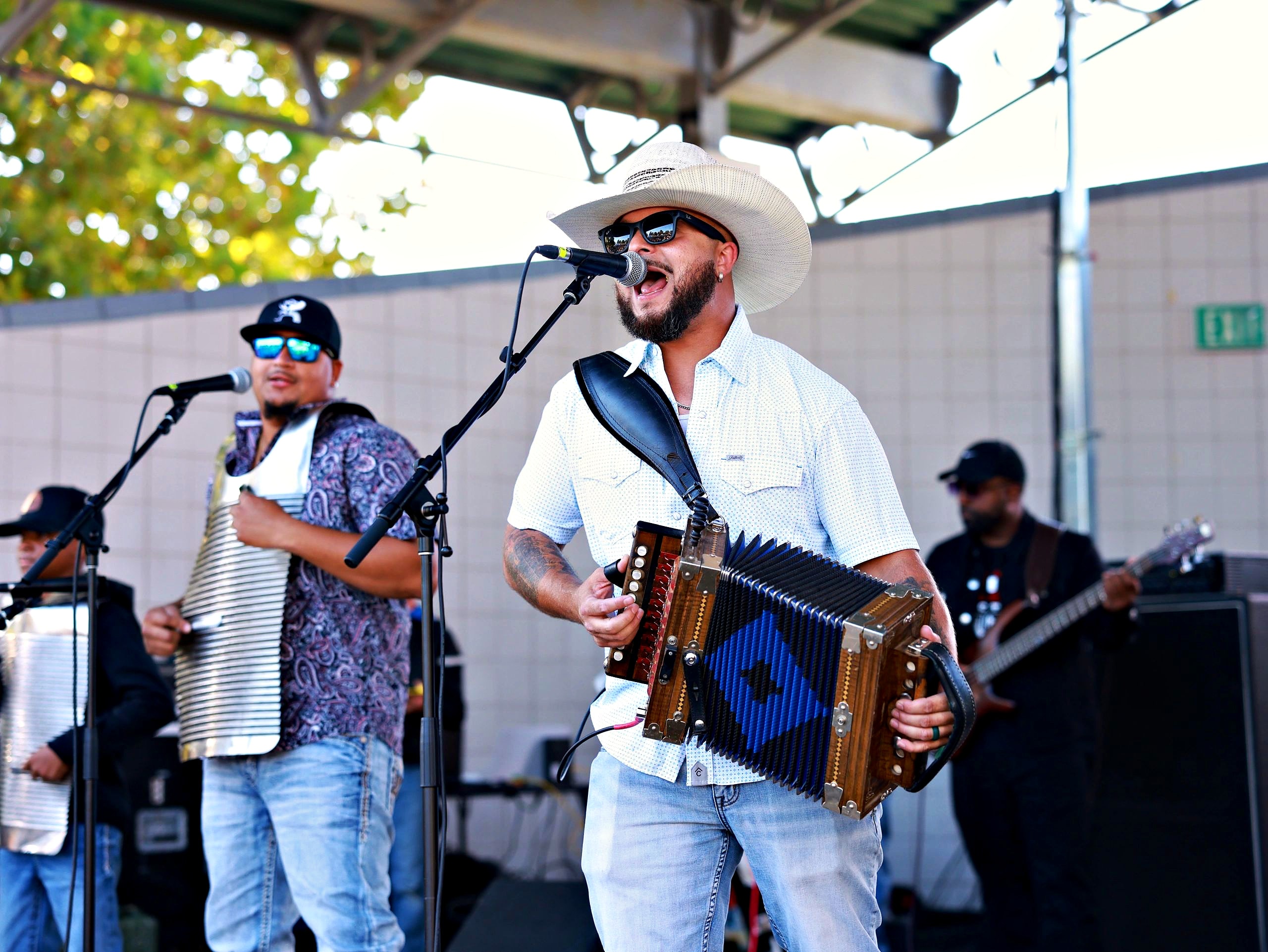 An accordion player in a white cowboy hat sings on stage with his Zydeco band